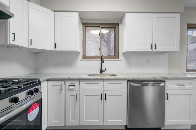 kitchen with wall chimney range hood, white cabinets, appliances with stainless steel finishes, and sink