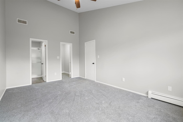 unfurnished bedroom featuring ceiling fan, carpet, a high ceiling, a spacious closet, and a baseboard radiator