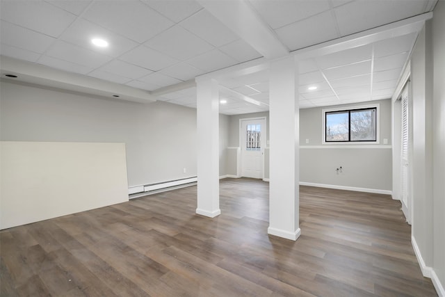 basement featuring wood-type flooring, a baseboard radiator, and a drop ceiling