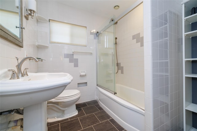 bathroom with tile walls, bath / shower combo with glass door, tile patterned floors, and toilet