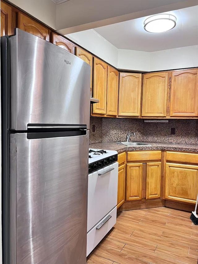 kitchen with white gas range, stainless steel fridge, light hardwood / wood-style floors, tasteful backsplash, and sink