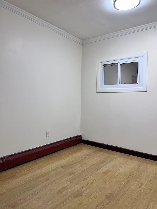 spare room with baseboard heating, light wood-type flooring, and crown molding