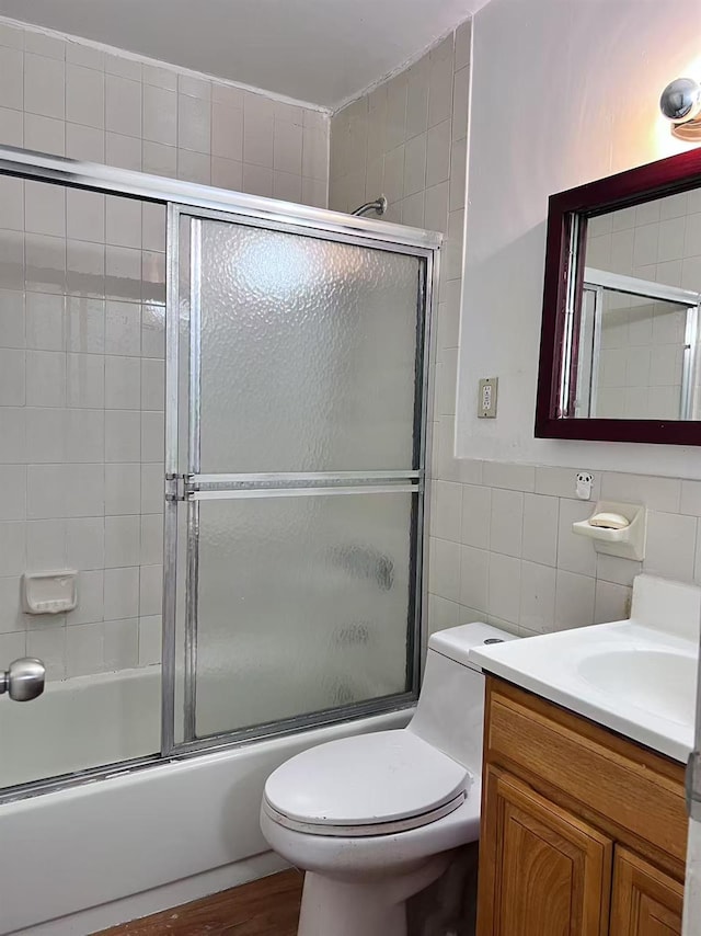 full bathroom featuring tile walls, shower / bath combination with glass door, vanity, and toilet