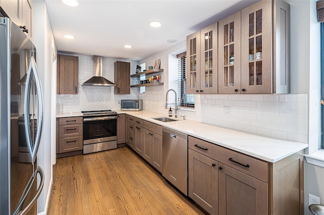 kitchen featuring stainless steel appliances, sink, light hardwood / wood-style flooring, backsplash, and wall chimney range hood