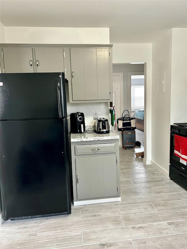 kitchen featuring black refrigerator, gray cabinets, and range