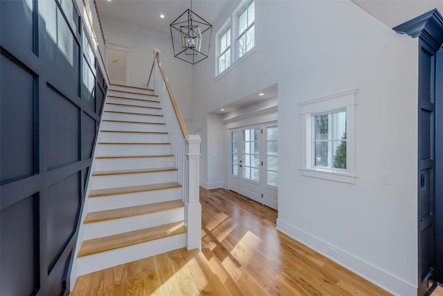 entrance foyer with a towering ceiling, crown molding, light wood-type flooring, french doors, and a chandelier