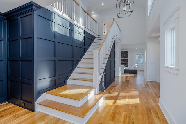 staircase with a fireplace, a notable chandelier, ornamental molding, and hardwood / wood-style flooring