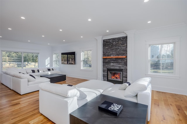 living room with light wood-type flooring, crown molding, plenty of natural light, and a stone fireplace