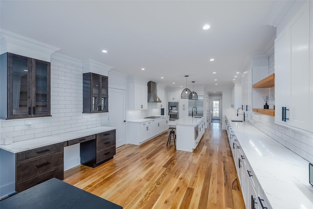 kitchen featuring white cabinetry, decorative backsplash, a kitchen island with sink, wall chimney exhaust hood, and sink