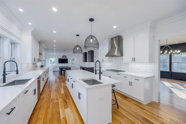 kitchen featuring sink, an island with sink, gas cooktop, and wall chimney range hood