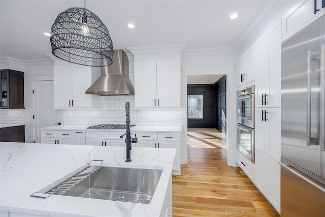 kitchen featuring decorative light fixtures, white cabinetry, light wood-type flooring, appliances with stainless steel finishes, and wall chimney exhaust hood