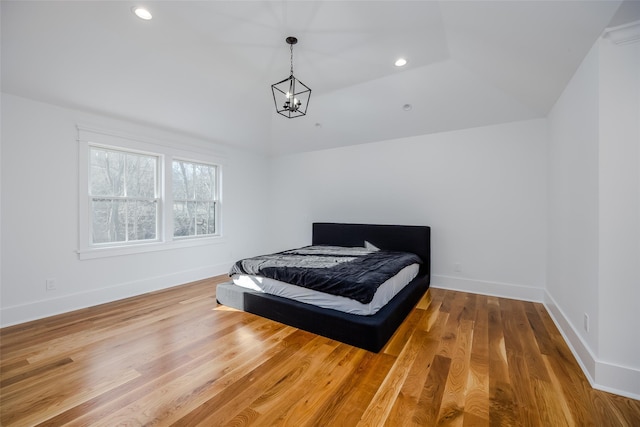 bedroom featuring an inviting chandelier, lofted ceiling, hardwood / wood-style flooring, and a tray ceiling