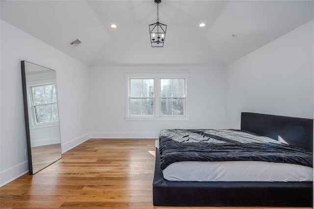 bedroom with lofted ceiling, multiple windows, a chandelier, and light hardwood / wood-style floors