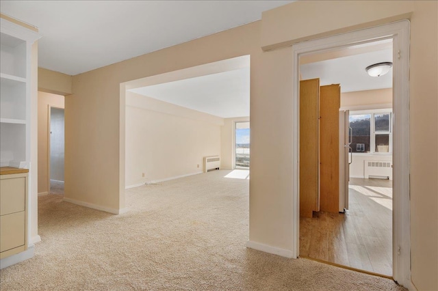 hall with plenty of natural light, radiator heating unit, and light carpet