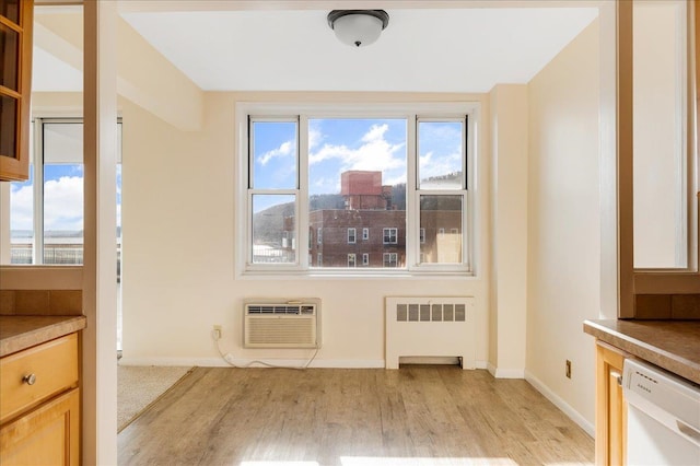 unfurnished dining area with radiator, a healthy amount of sunlight, a wall mounted AC, and light hardwood / wood-style flooring