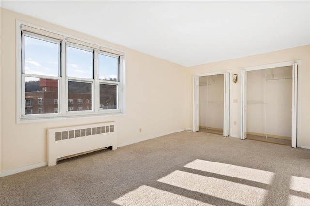 unfurnished bedroom featuring carpet floors, radiator heating unit, and two closets