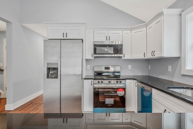 kitchen featuring hardwood / wood-style floors, lofted ceiling, white cabinetry, stainless steel appliances, and dark stone countertops