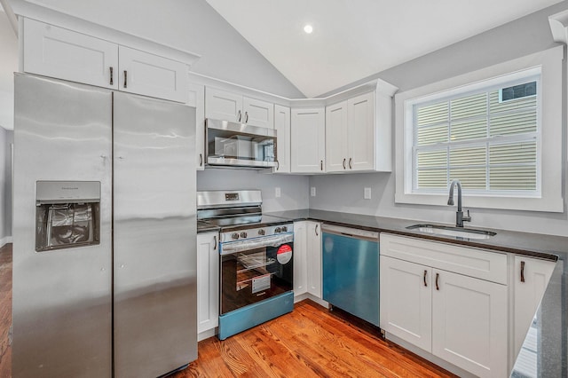 kitchen with white cabinets, lofted ceiling, stainless steel appliances, sink, and light wood-type flooring