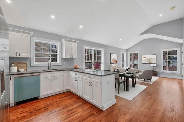 kitchen with kitchen peninsula, dishwashing machine, lofted ceiling, white cabinets, and sink