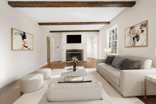 living room featuring beamed ceiling, light hardwood / wood-style flooring, and a fireplace