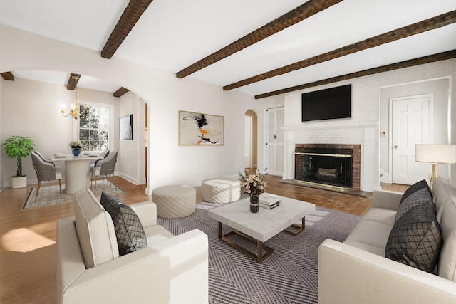 living room with a brick fireplace, hardwood / wood-style floors, beam ceiling, and a chandelier