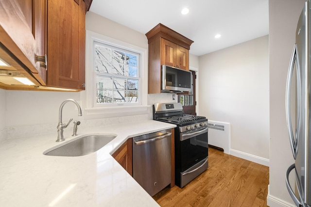 kitchen with sink, radiator heating unit, light hardwood / wood-style flooring, and appliances with stainless steel finishes