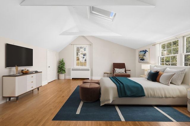 bedroom featuring hardwood / wood-style flooring, lofted ceiling with skylight, radiator, and multiple windows