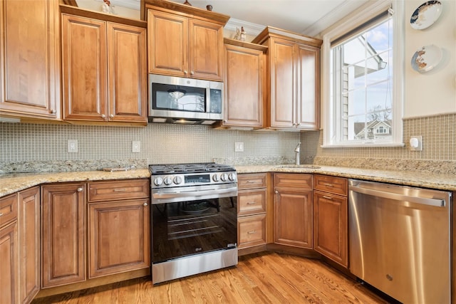 kitchen featuring light stone countertops, backsplash, appliances with stainless steel finishes, ornamental molding, and sink