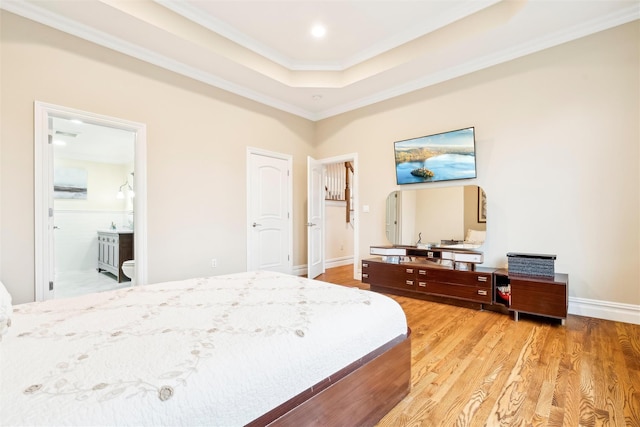 bedroom with ornamental molding, a raised ceiling, light hardwood / wood-style floors, and connected bathroom