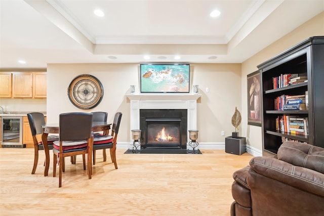 living room with beverage cooler, a tray ceiling, crown molding, and light hardwood / wood-style flooring