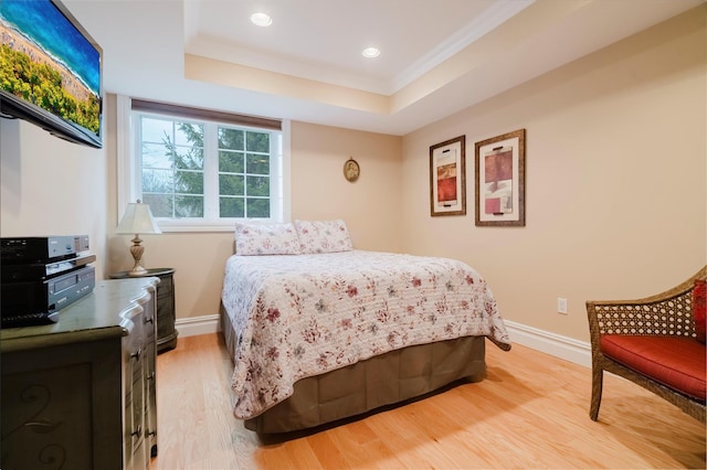 bedroom with a raised ceiling, light wood-type flooring, and crown molding