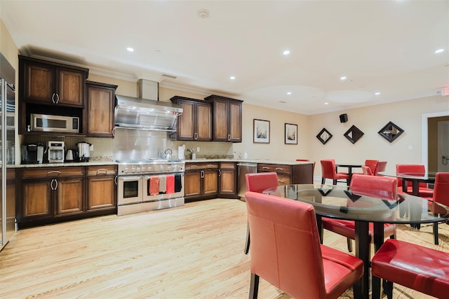 kitchen with stainless steel appliances, light hardwood / wood-style floors, decorative backsplash, dark brown cabinetry, and wall chimney range hood