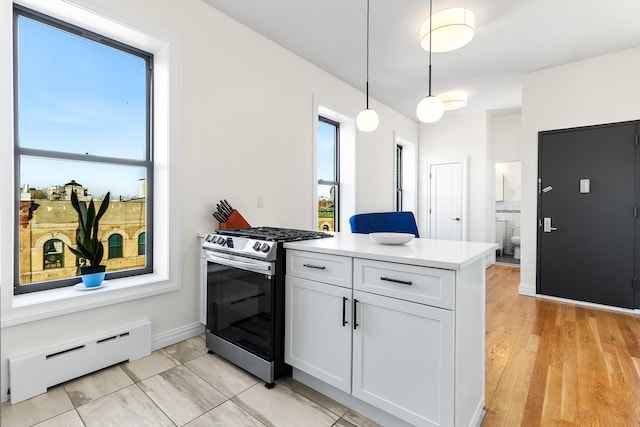 kitchen featuring stainless steel gas range, hanging light fixtures, baseboard heating, kitchen peninsula, and white cabinets