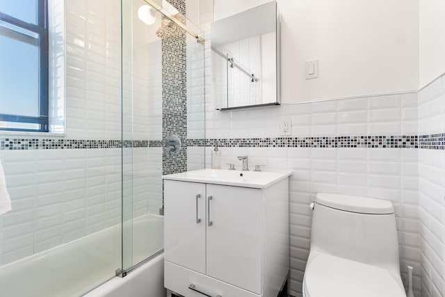 full bathroom featuring vanity, toilet, combined bath / shower with glass door, and tile walls