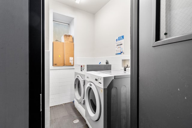 clothes washing area featuring tile walls, dark tile patterned floors, and washing machine and clothes dryer