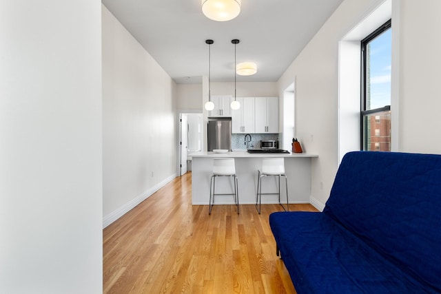 kitchen with a breakfast bar, refrigerator, white cabinets, decorative light fixtures, and kitchen peninsula