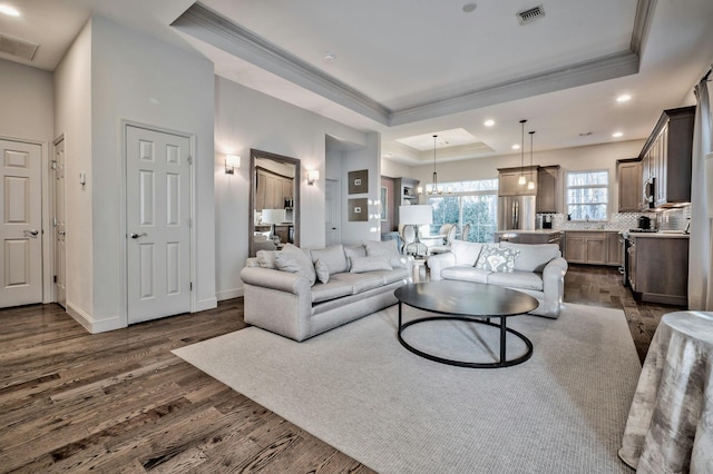 living room with a notable chandelier, a tray ceiling, crown molding, and dark hardwood / wood-style flooring