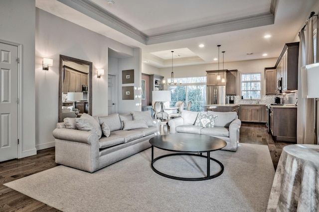 living room featuring a raised ceiling, ornamental molding, a notable chandelier, and dark hardwood / wood-style floors