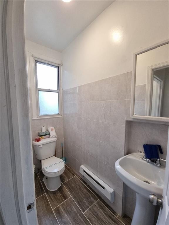 bathroom with a baseboard radiator, lofted ceiling, sink, tile walls, and toilet