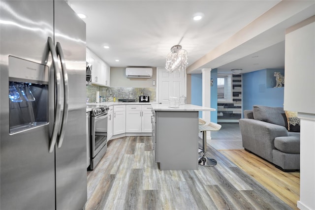 kitchen featuring decorative light fixtures, an AC wall unit, a breakfast bar, stainless steel appliances, and white cabinets