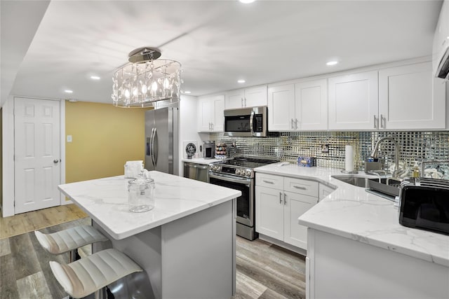 kitchen with pendant lighting, appliances with stainless steel finishes, white cabinetry, sink, and light stone counters