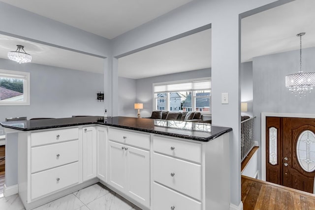 kitchen featuring an inviting chandelier, white cabinetry, dark stone countertops, kitchen peninsula, and pendant lighting