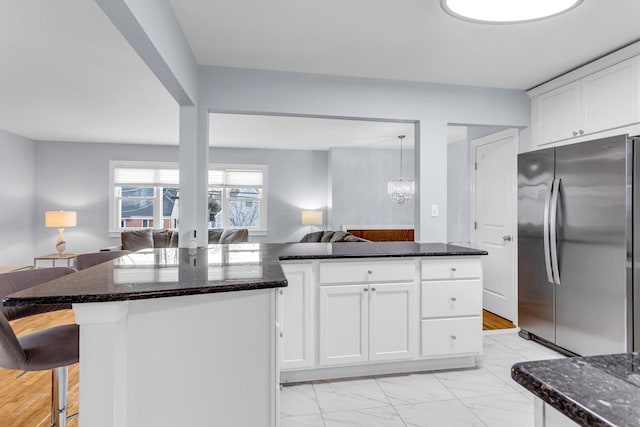 kitchen featuring decorative light fixtures, white cabinets, a center island, dark stone counters, and stainless steel fridge