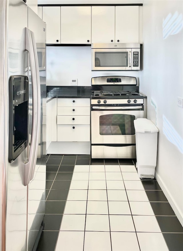 kitchen with stainless steel appliances, dark tile patterned floors, and white cabinetry