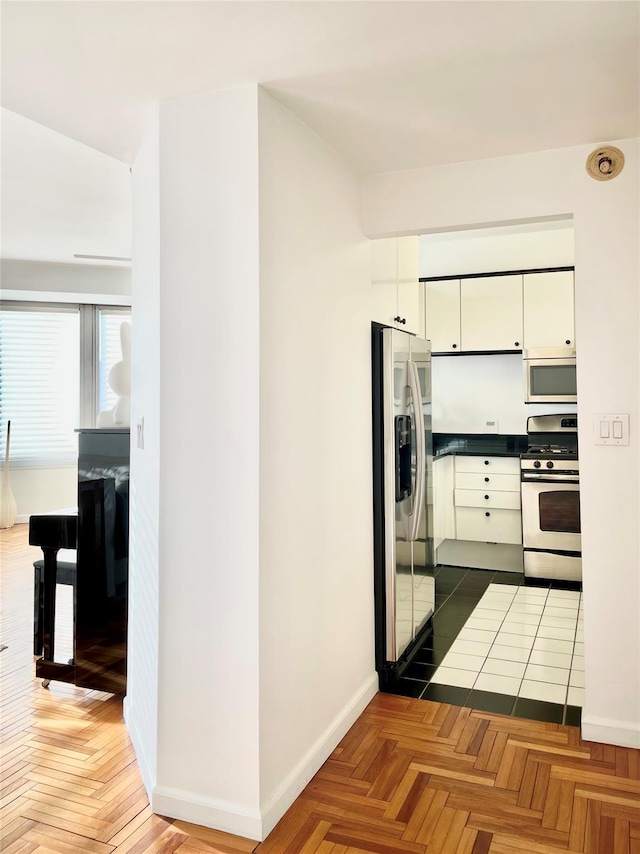 kitchen with dark parquet flooring, appliances with stainless steel finishes, and white cabinetry