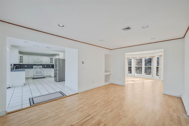 unfurnished living room featuring light wood-type flooring, a sink, visible vents, and crown molding