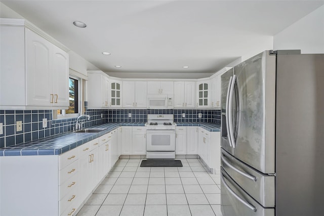 kitchen with light tile patterned floors, white appliances, a sink, backsplash, and tile counters