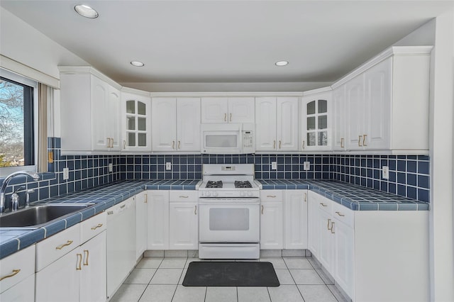 kitchen with tile countertops, white appliances, white cabinetry, and a sink