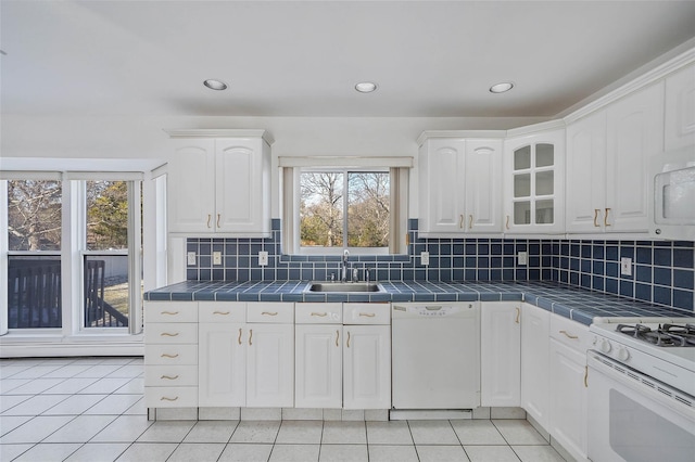 kitchen with light tile patterned floors, tile counters, white cabinetry, a sink, and white appliances