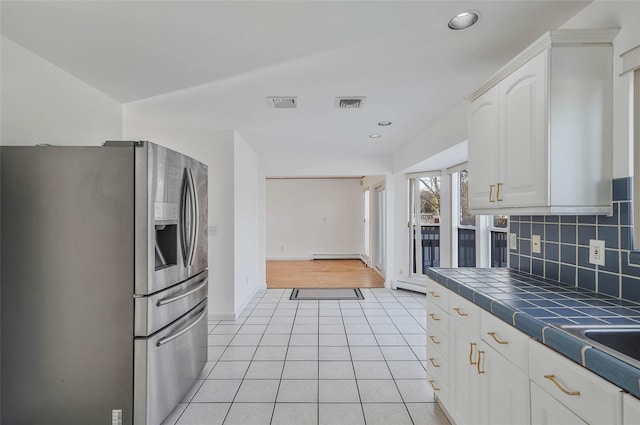 kitchen with light tile patterned floors, visible vents, backsplash, tile counters, and stainless steel fridge